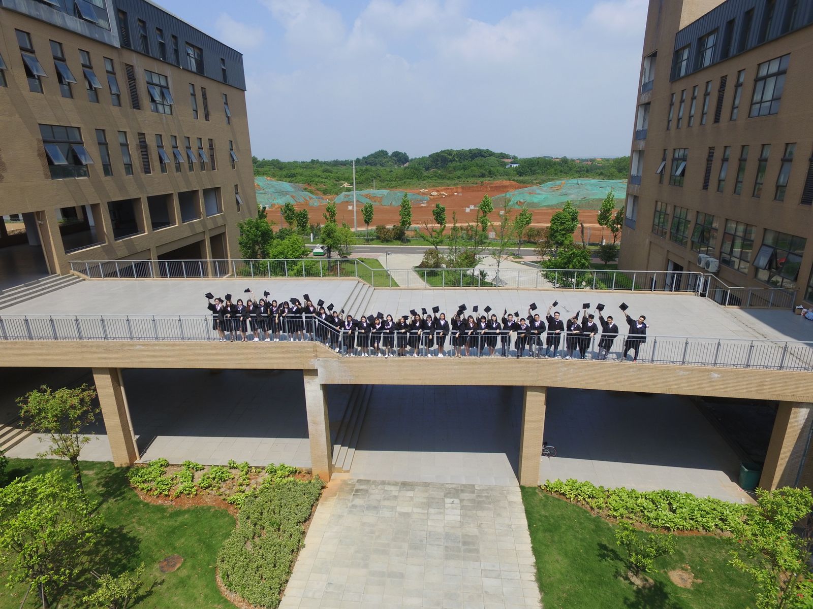 Aerial view of graduates in gowns crossing a bridge between campus buildings