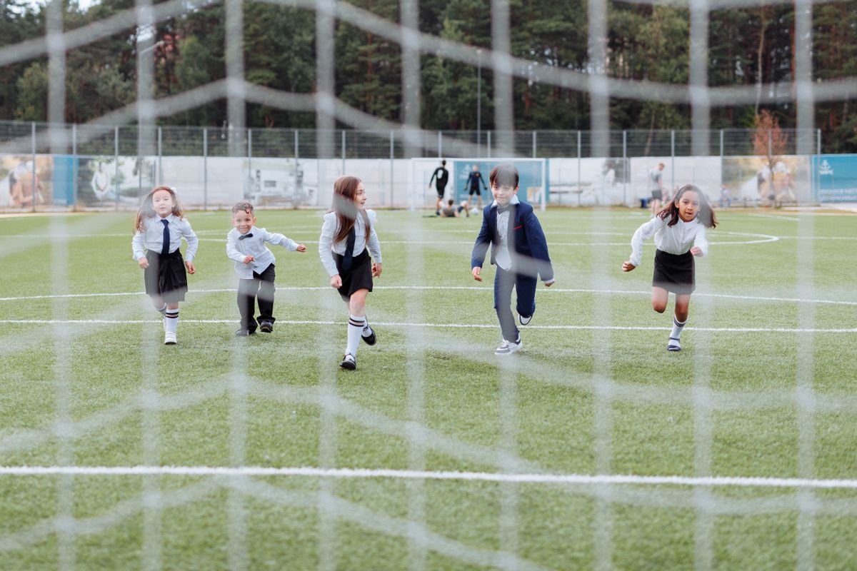 Children in school uniforms playing football on a grass field