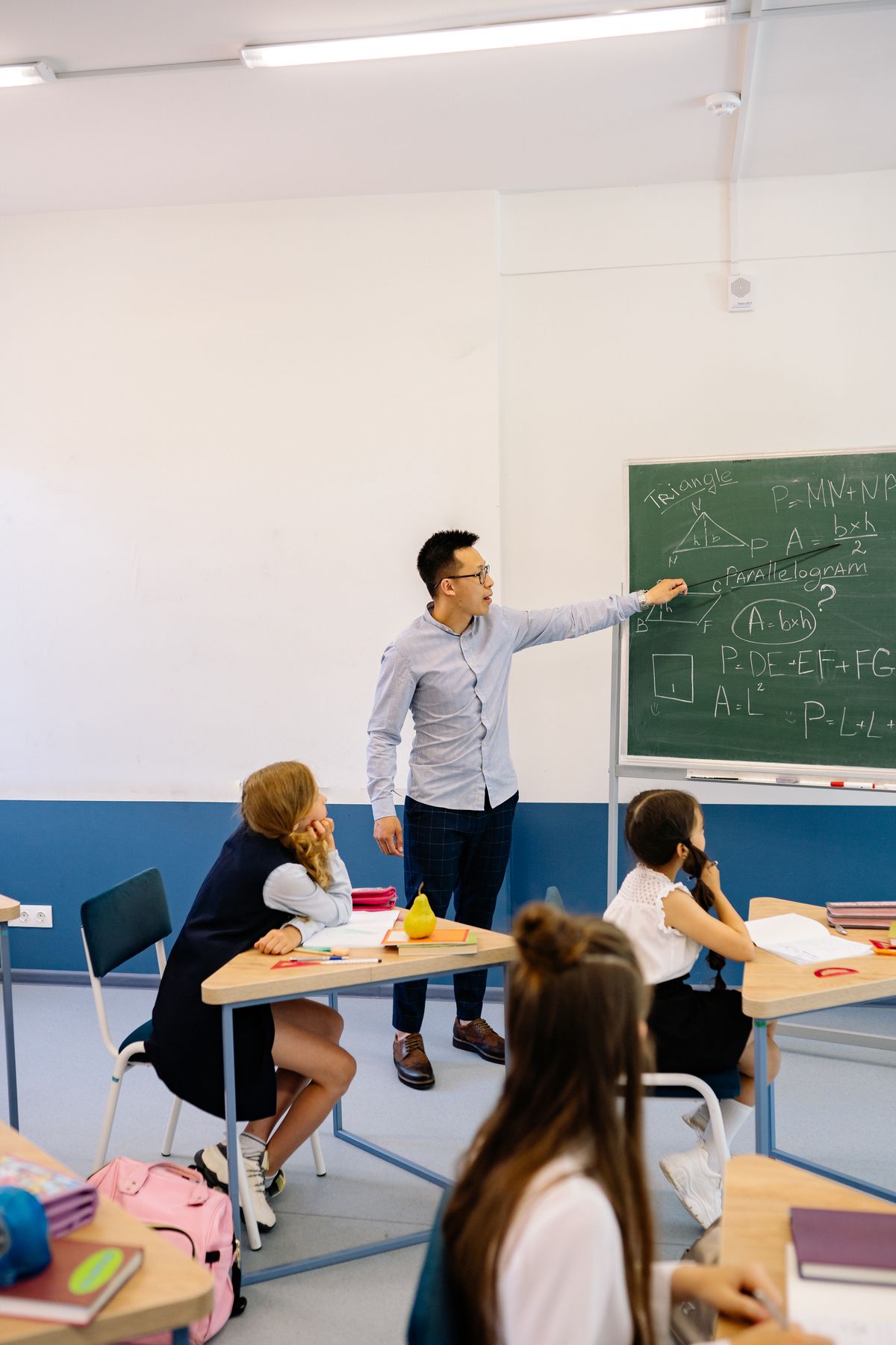 Teacher pointing to equations written on a classroom blackboard
